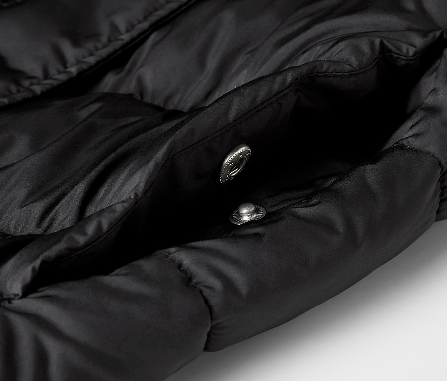 Gros plan sur une veste noire matelassée avec une poche ouverte et deux boutons-pression argentés.