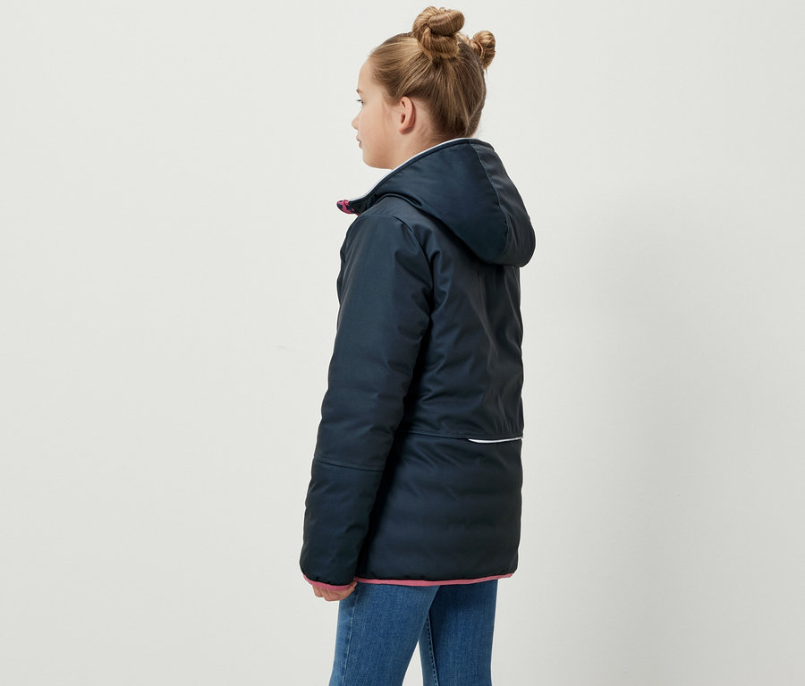 Une fille se tient de côté et porte une veste softshell et matelassée 2-en-1 bleue pour enfants.