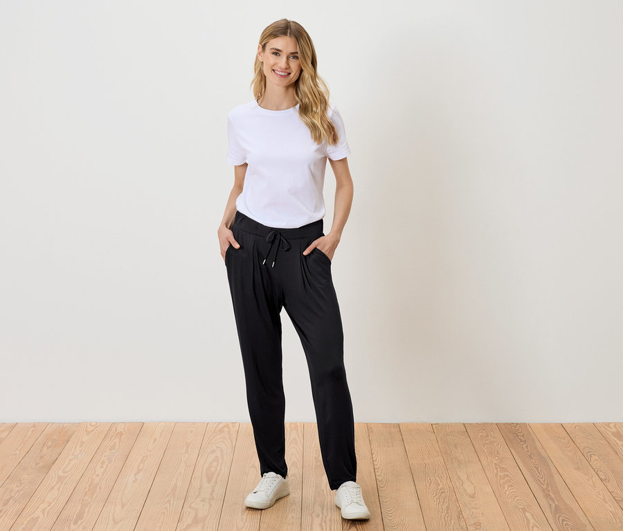 Femme blonde portant un t-shirt blanc, un pantalon noir et des baskets blanches.