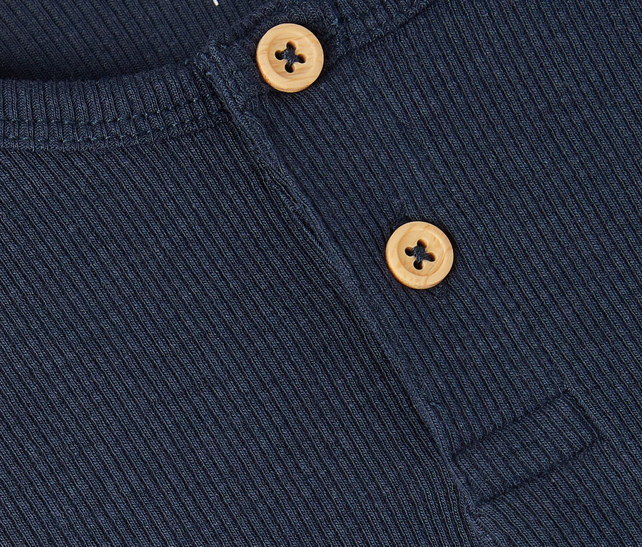 Gros plan d'une chemise bleu marine côtelée avec deux boutons marron clair et le nom "name it" dans le coin supérieur gauche.