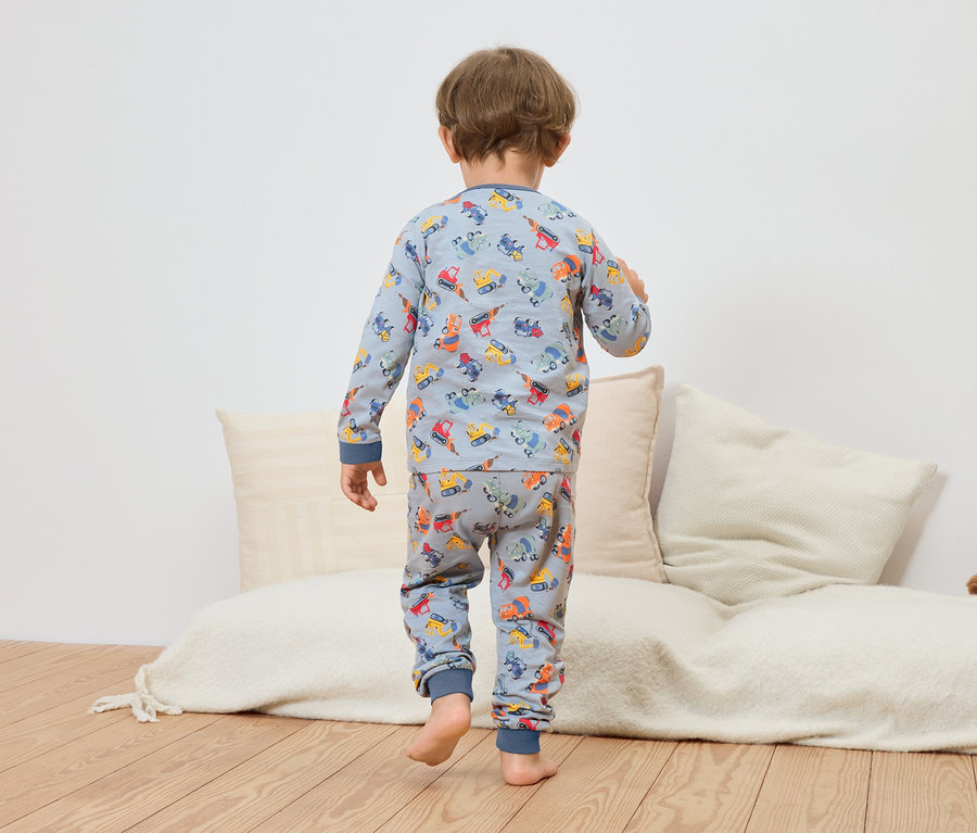 Un enfant, vu de dos, porte un pyjama bleu avec un motif de travaux de construction.