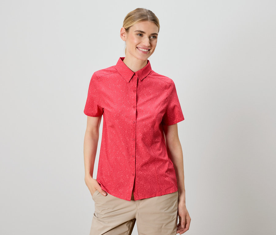 Une femme porte une chemise rouge à manches courtes et un pantalon beige.