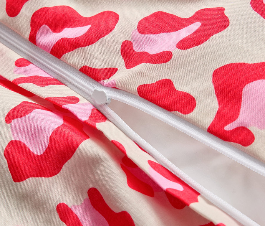 Gros plan d'une fermeture éclair partiellement ouverte sur un tissu avec des taches roses et rouges.