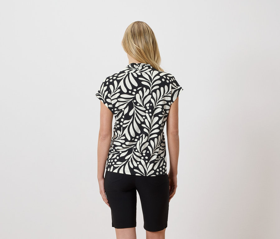 Vue de dos d'une femme blonde portant un chemisier noir et blanc à motif de feuilles et un short noir.