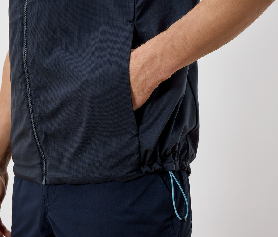 Gros plan d'une personne portant un gilet et un pantalon bleu marine, avec une main dans la poche du gilet.