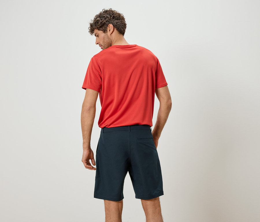 Homme vu de dos, portant un t-shirt rouge et un short bleu sur fond blanc.