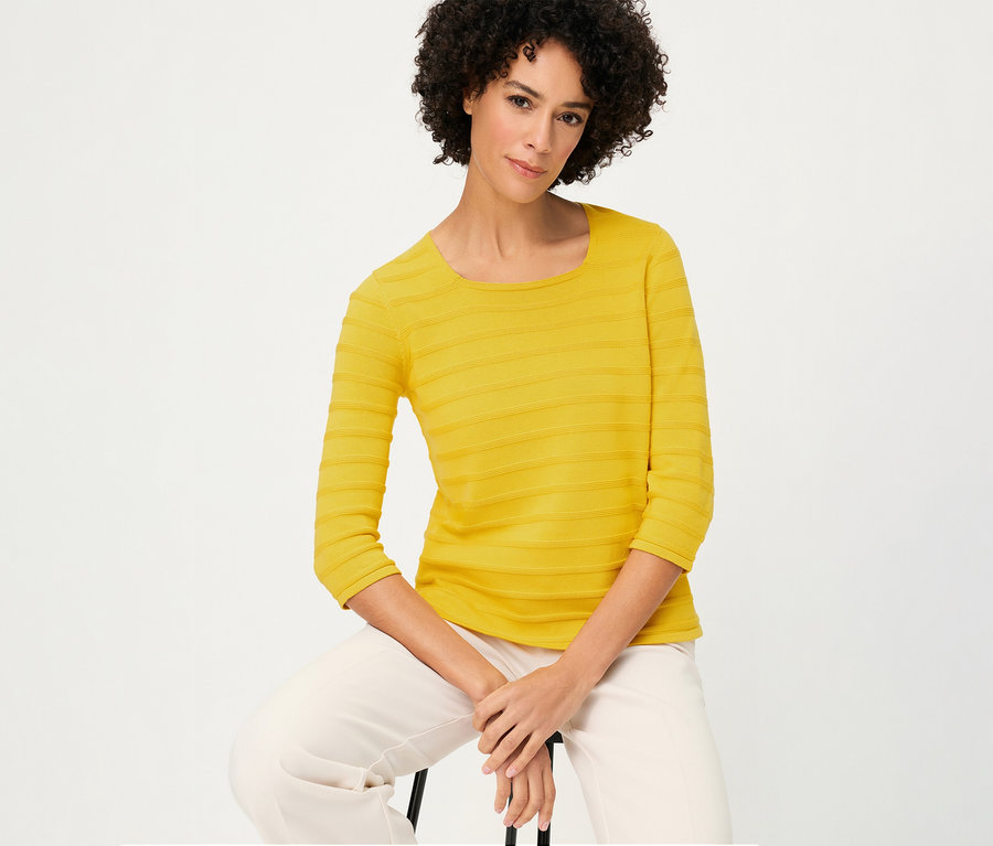 Une femme est assise et porte un pull-over structuré Olsen à manches 3/4 jaune et un pantalon clair.