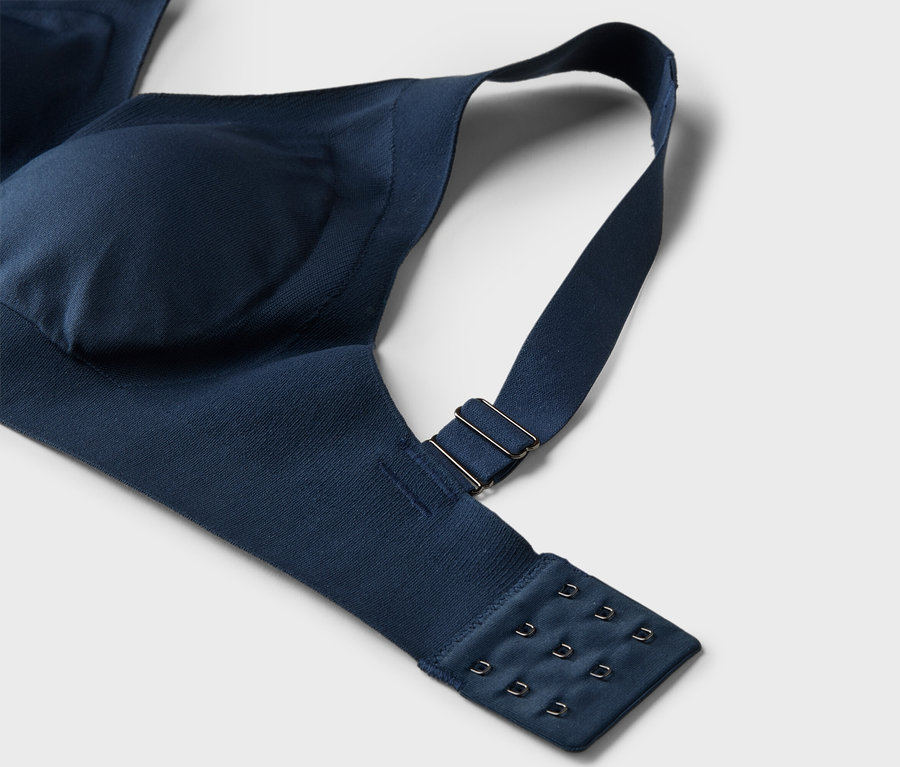 Gros plan d'un soutien-gorge bleu marine avec bretelle réglable et fermeture à agrafes sur fond blanc.