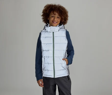 Un garçon avec un afro se tient sur un fond gris dans un gilet réfléchissant à capuche sur un pull bleu et un pantalon gris.