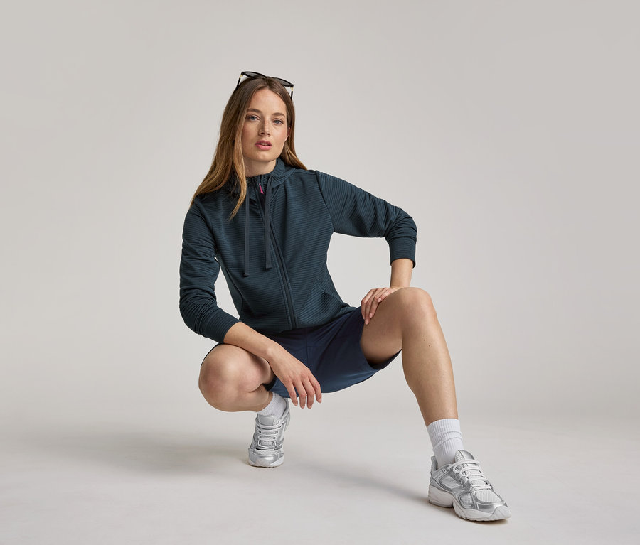 Femme accroupie en veste à capuche et short bleu marine. La veste à capuche est bleu marine.