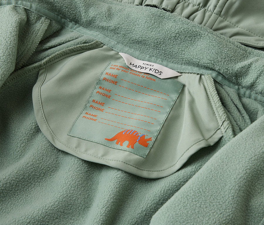 Vue intérieure d'une veste vert clair Tchibo Happy Kids avec étiquette nominative et motif tricératops.