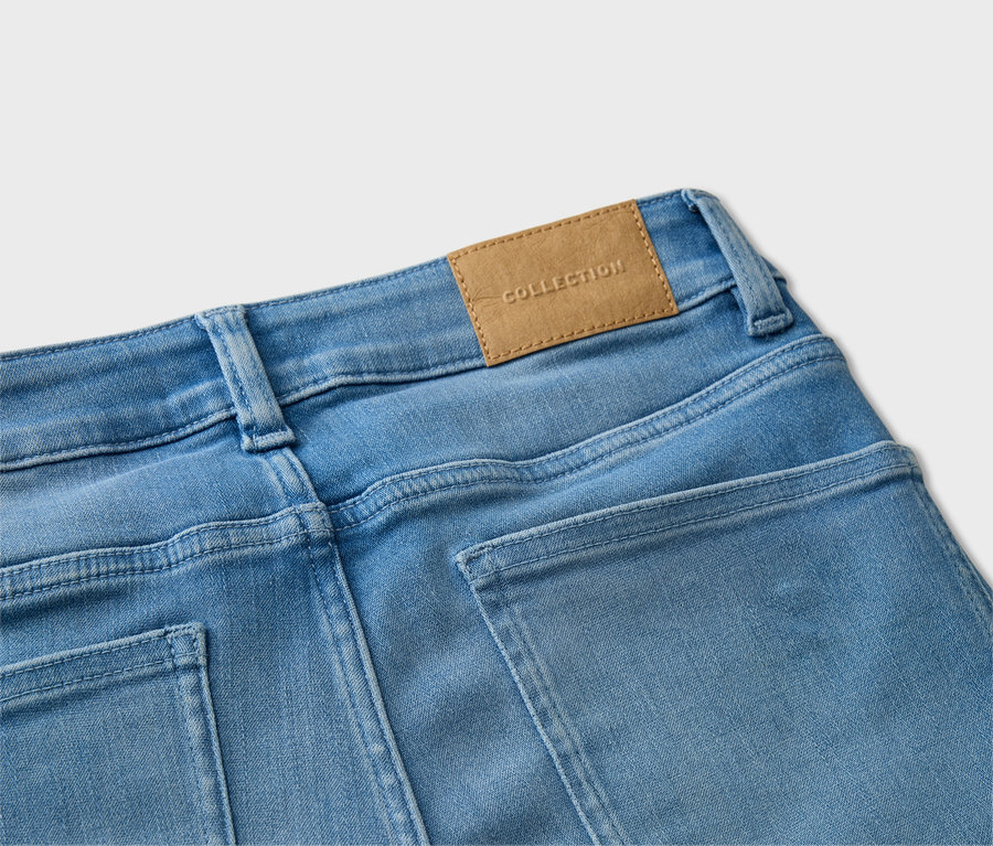 Gros plan sur l'arrière d'un jean bleu clair avec une étiquette marron portant l'inscription 'Collection'.