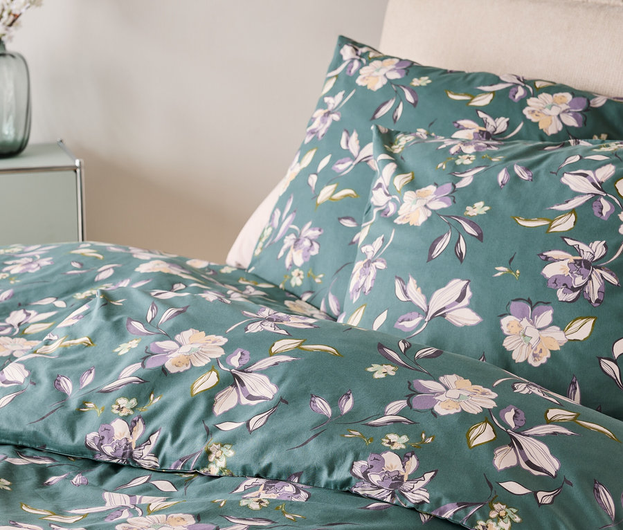 Gros plan de linge de lit à motif floral dans les tons de vert, violet et blanc.