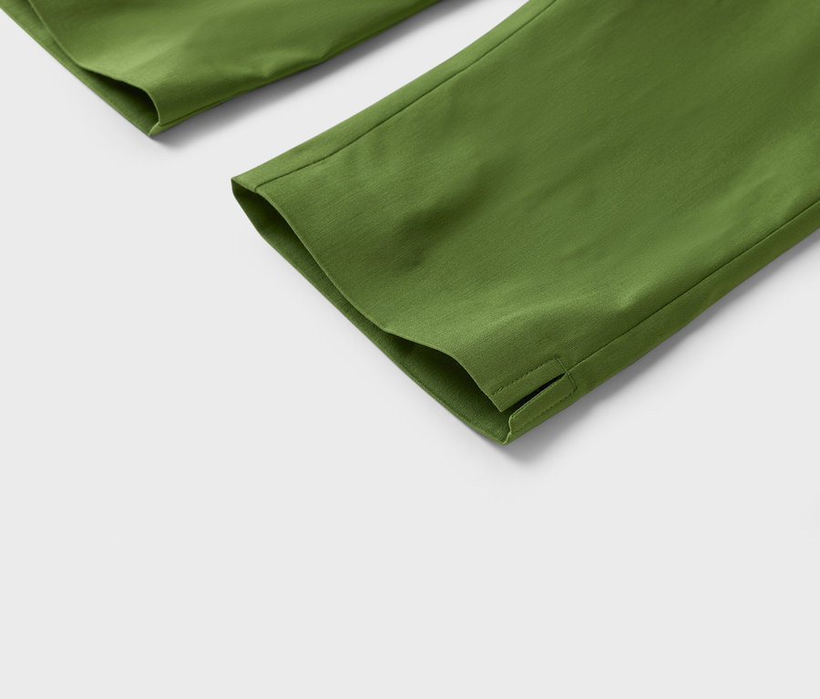 Gros plan sur le bas de jambes de pantalon vert olive avec fente à l'ourlet sur fond blanc.
