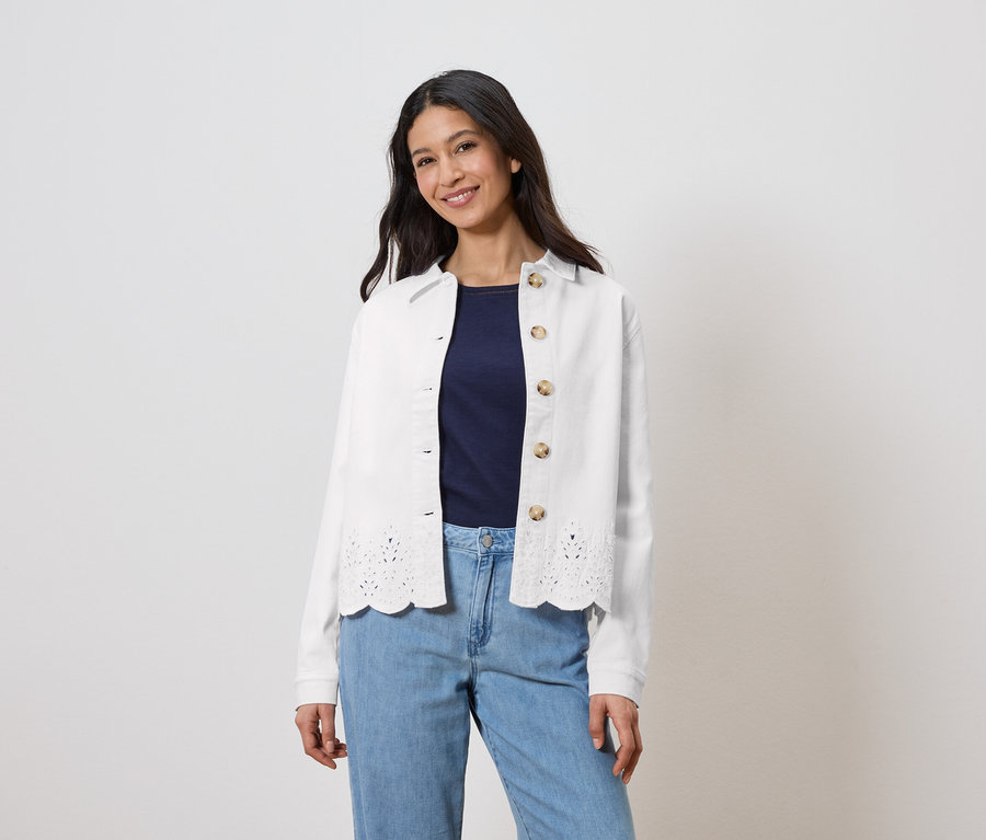 Une femme porte une veste blanche à motifs ajourés sur un haut bleu marine et un jean bleu clair.