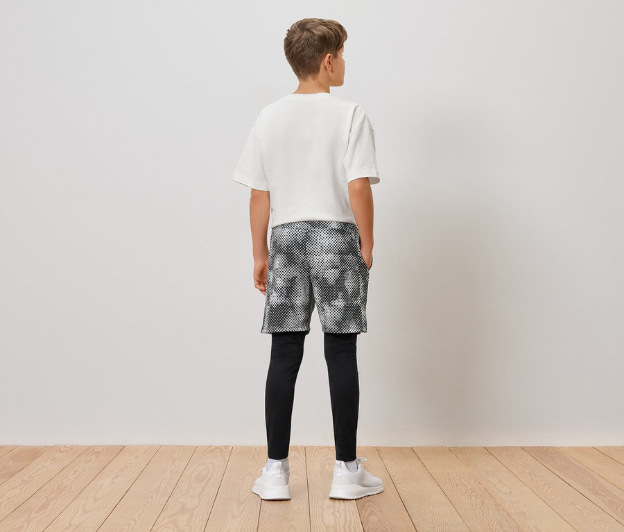 Vue de dos d'un garçon portant un t-shirt blanc, un short à motifs, des leggings noirs et des baskets blanches.