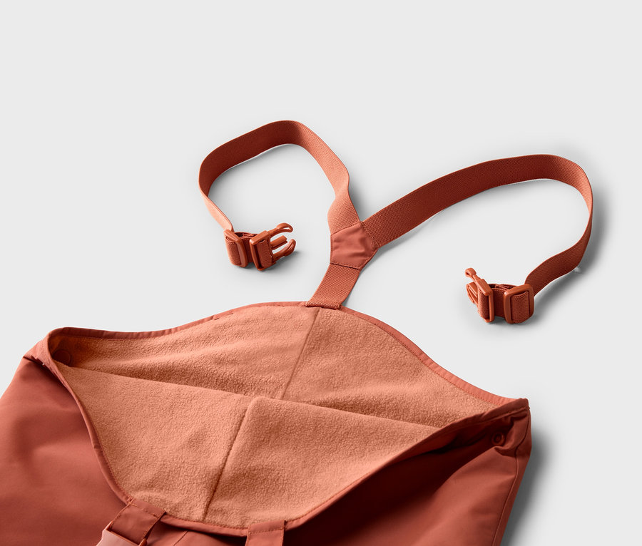 Gros plan d'un pantalon orange à bretelles et boucles sur fond blanc.