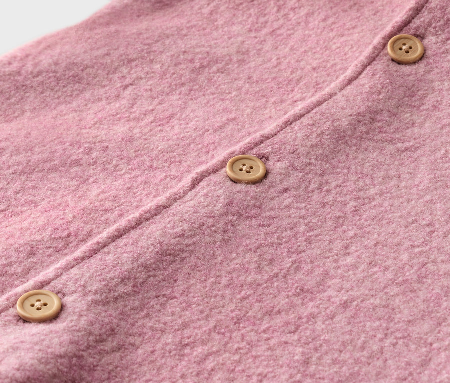 Gros plan d'un tissu tricoté rose avec trois boutons marron clair.