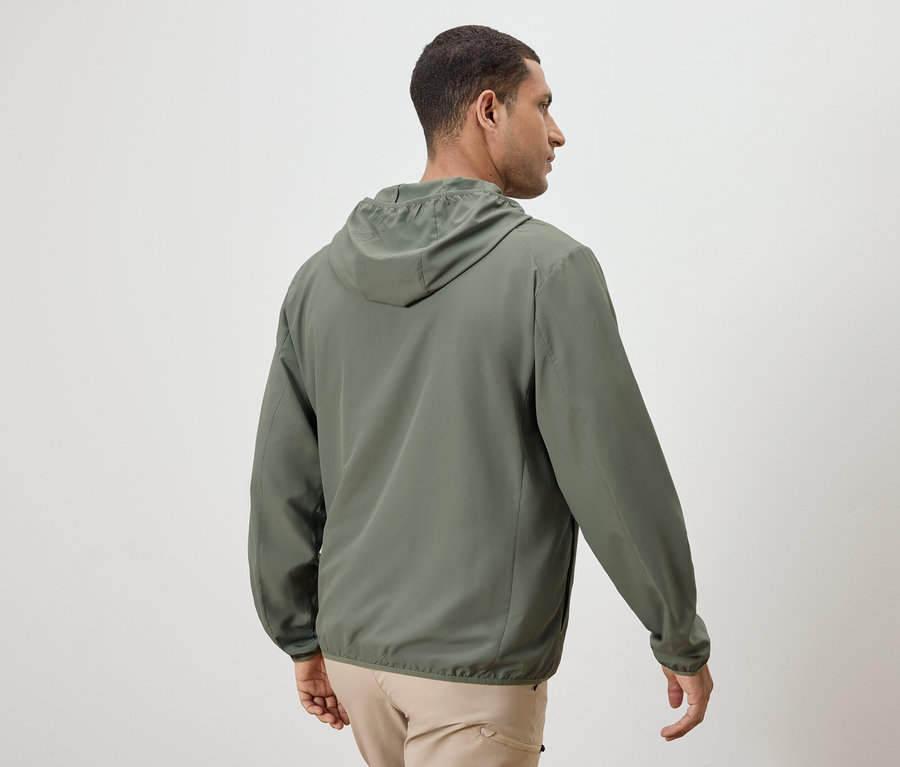 Homme vu de dos, portant une veste à capuche vert olive et un pantalon beige.