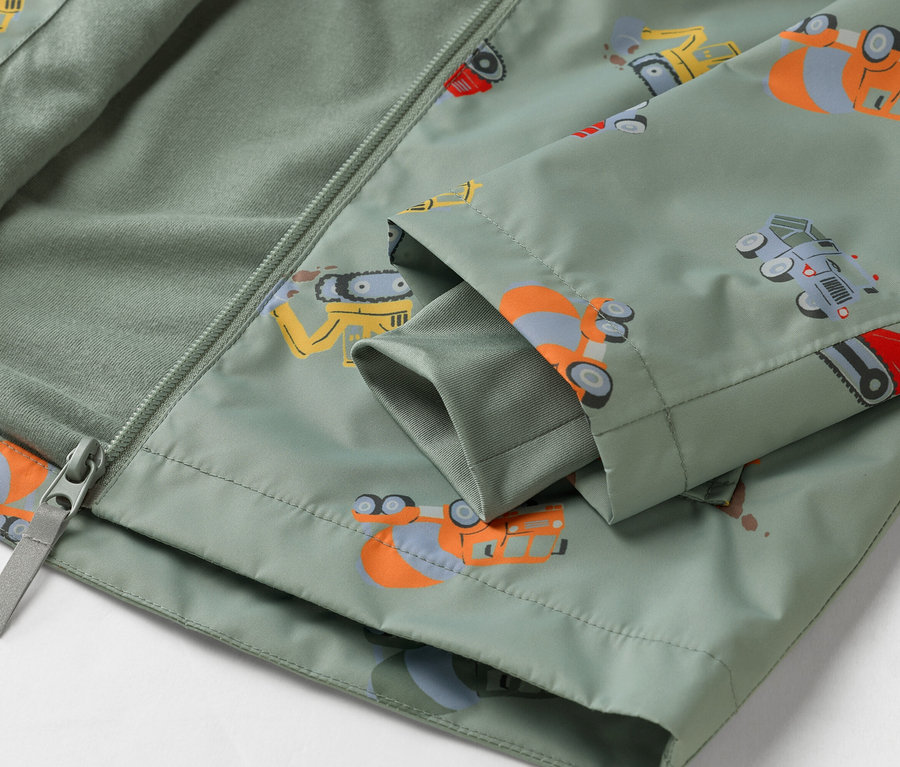 Gros plan sur une veste vert olive à motif de véhicules de chantier, partiellement ouverte avec une fermeture éclair.