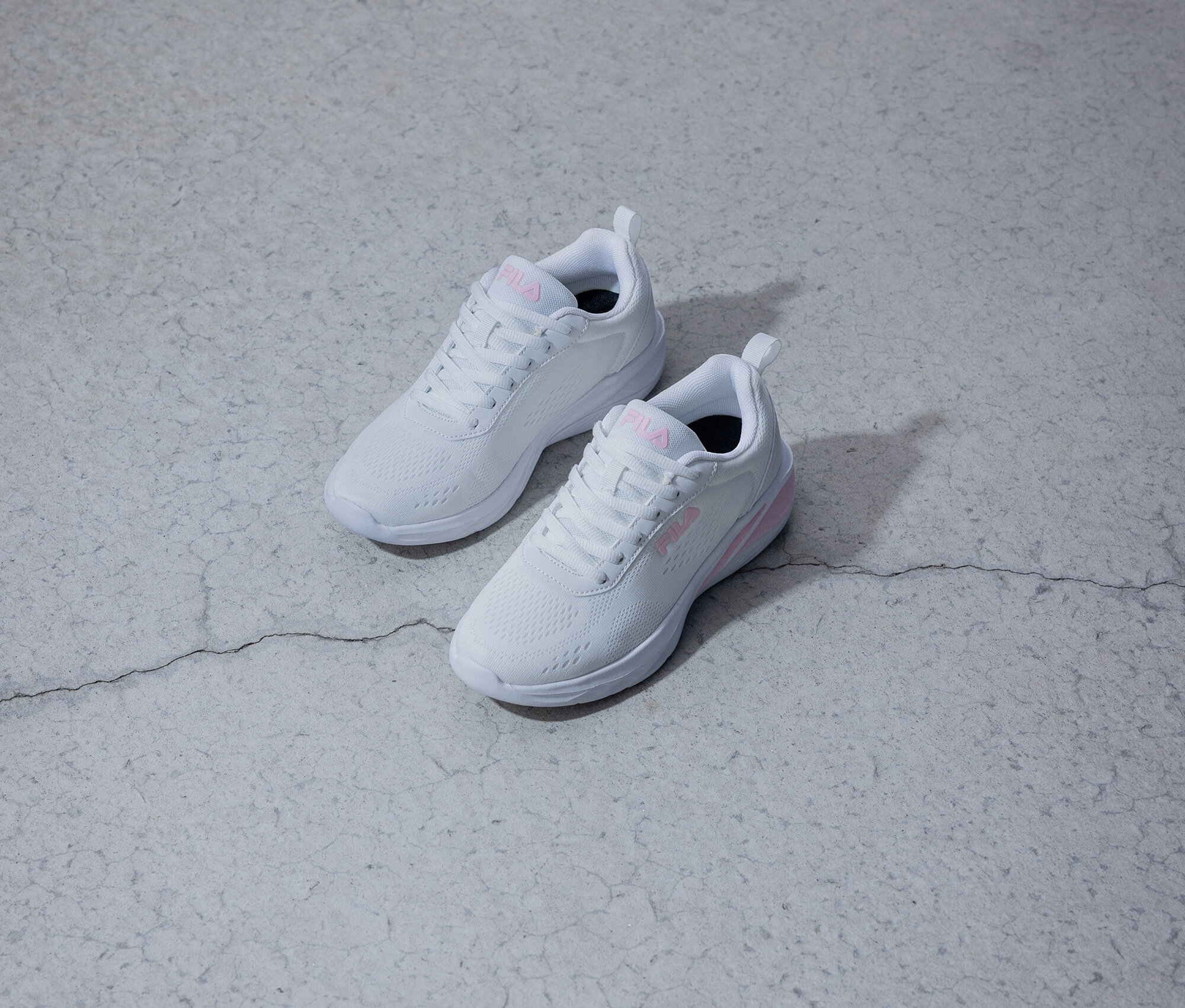 Deux baskets blanches Fila avec un logo rose sont posées sur un fond gris.
