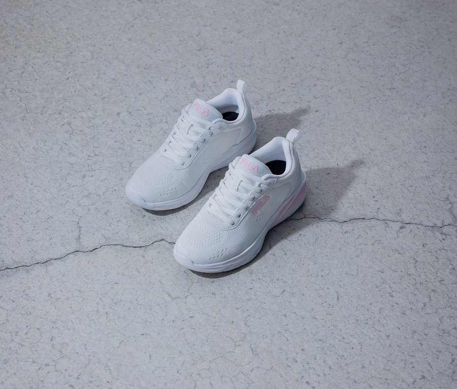 Deux baskets blanches Fila avec un logo rose sont posées sur un fond gris.