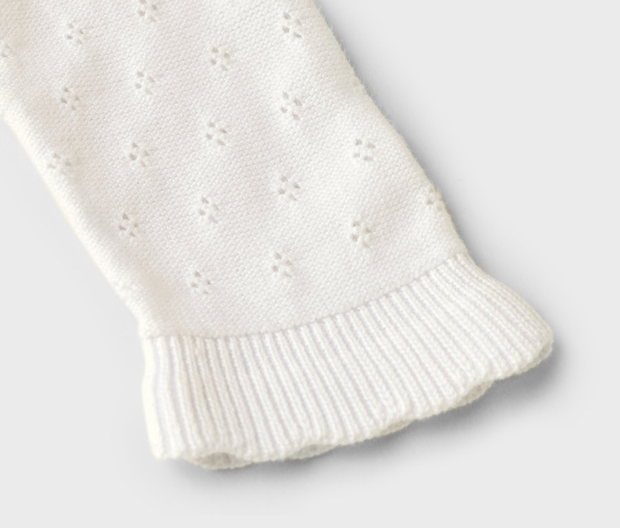 Manche d'un pull en tricot blanc avec motif ajouré et ourlet à volants, gros plan.