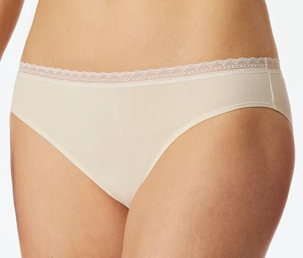Une personne porte un slip Rio SCHIESSER beige avec une délicate bordure en dentelle blanche à la taille.