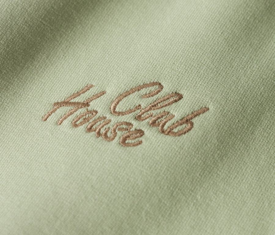 Gros plan d'un tissu vert clair avec la broderie marron "House Club".