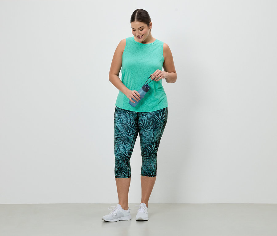 Une femme en tenue de sport tient une bouteille d'eau bleue. Elle porte un débardeur vert et un legging à motif turquoise.