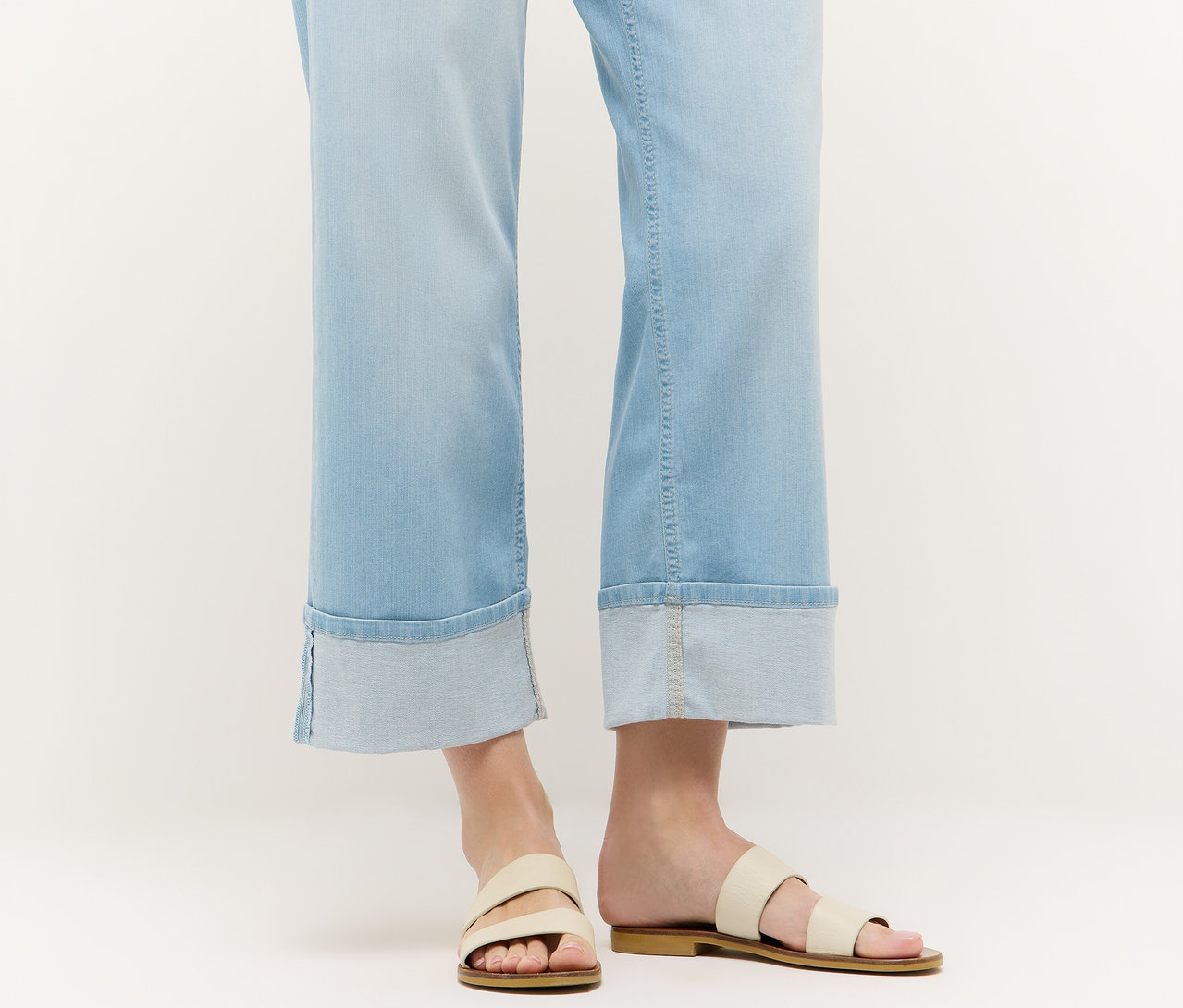 Gros plan sur des jambes portant un jean Angels Denim «
Laia Turn-Up
», Wide Leg, bleu clair et des sandales sur fond blanc.