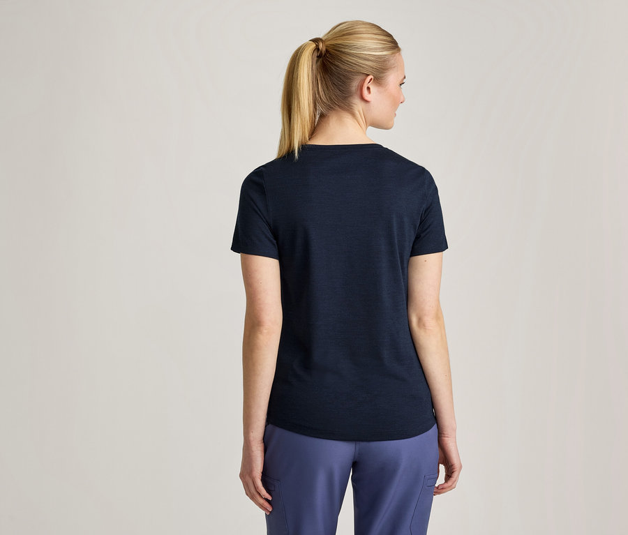 Femme vue de dos, avec des cheveux blonds en queue de cheval, portant un t-shirt bleu foncé et un pantalon bleu clair.