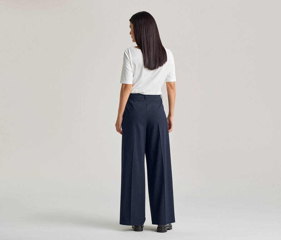 Vue arrière d'une femme aux longs cheveux foncés portant un t-shirt blanc et un pantalon large bleu marine avec ceinture.