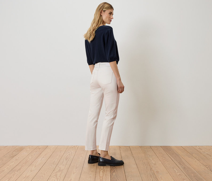 Femme debout, dos tourné, portant un haut bleu marine, un jean rose et des chaussures noires.