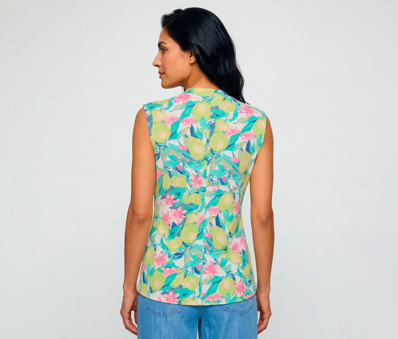 Femme de dos, légèrement tournée, portant un Olsen Shirt sans manches à motif de citrons verts et de fleurs avec un jean bleu.