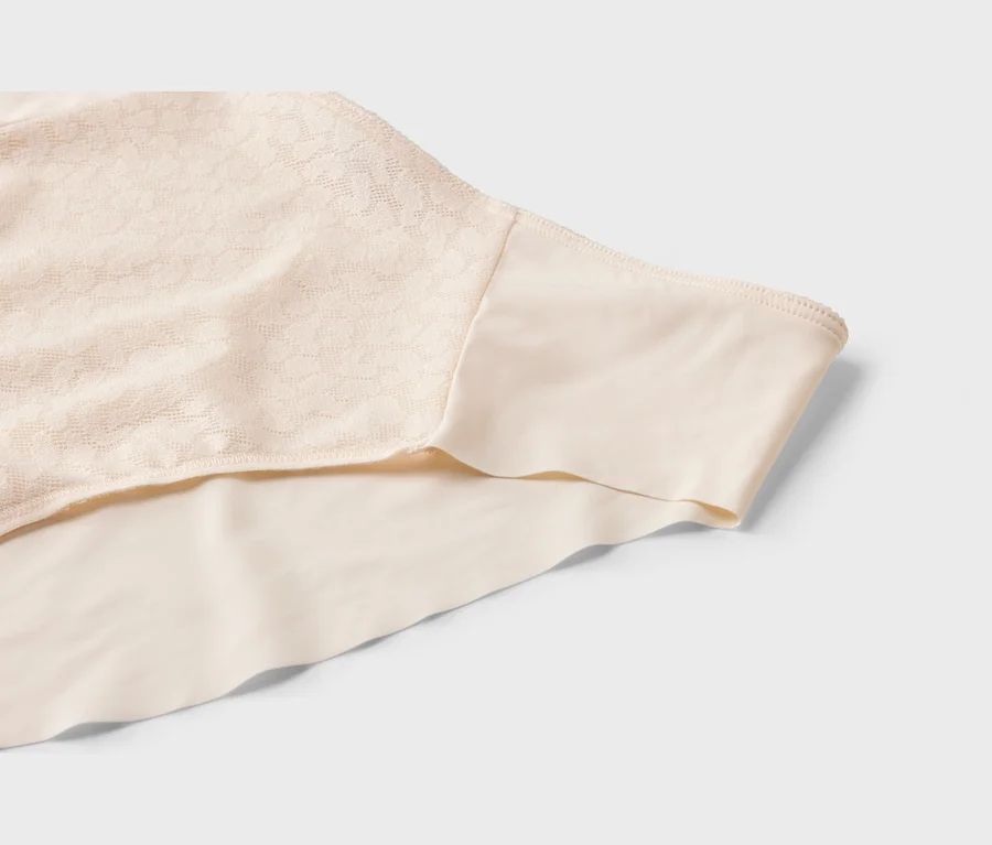 Gros plan d'un vêtement beige, probablement un sous-vêtement, présentant une section de tissu à motif dentelle à côté d'un tissu lisse et sans couture.