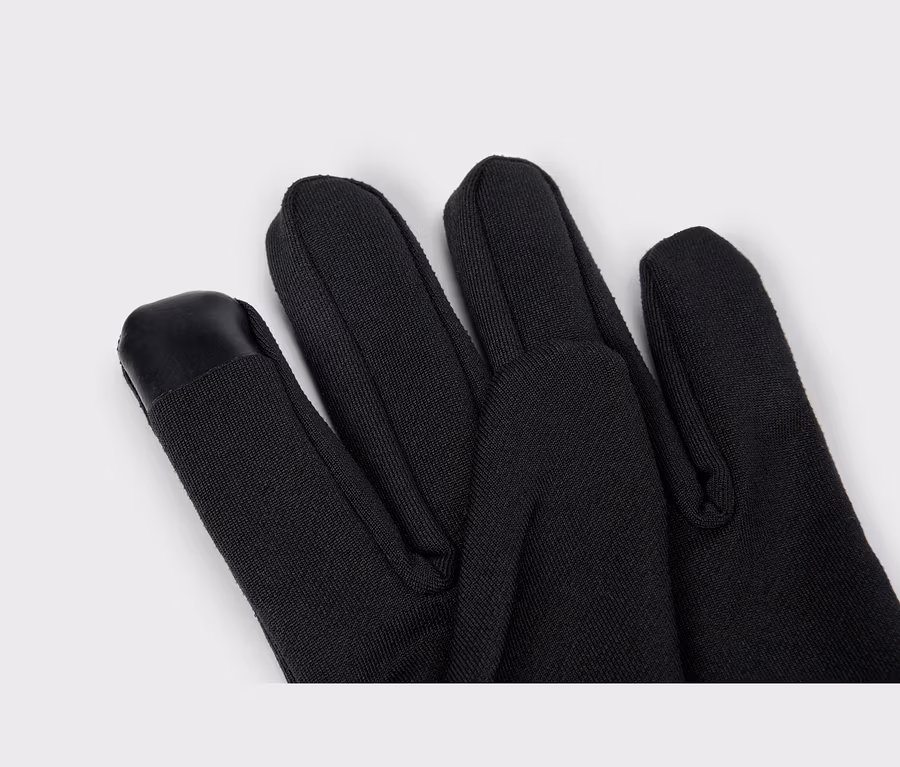 Gros plan sur un gant noir, montrant les doigts, avec un patch noir compatible écran tactile sur le bout de l'index.