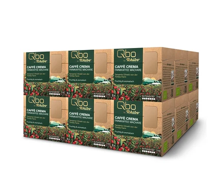 Pile de boîtes en carton marron de capsules de café Qbo by Tchibo Caffè Crema FARMKAFFEE MACHARE. Chaque boîte contient 8 capsules et présente des plants de café, le texte "Tansania | Direkt von der Tchibo Farm", "Fruchtig & aromatisch" et "Intensität 7/10".