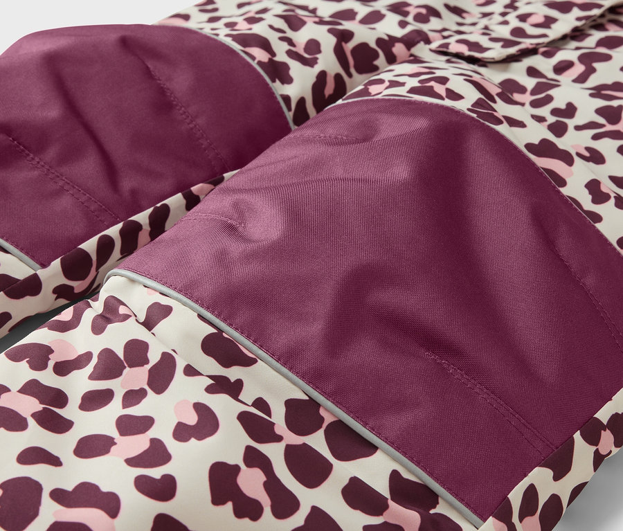 Gros plan d'un vêtement à motif léopard beige, violet foncé et rose. Il présente des empiècements violet foncé sur les genoux/coudes avec des bandes réfléchissantes.