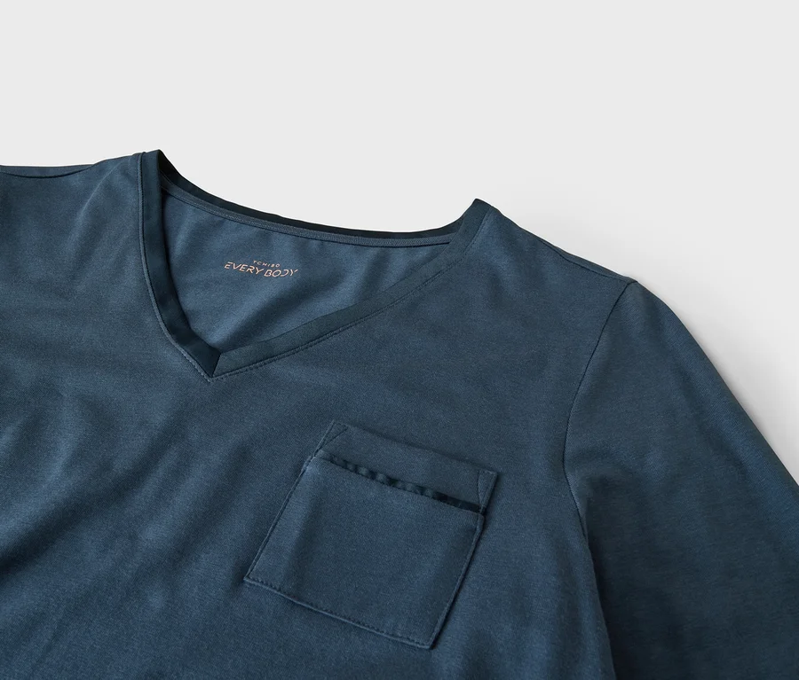 T-shirt bleu foncé à col en V avec une poche poitrine ornée d'une bordure noire. L'étiquette intérieure du col indique "TCHIBO EVERY BODY".
