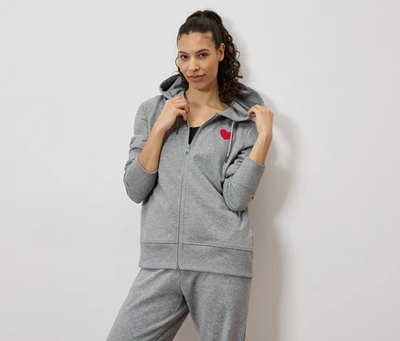 Femme portant un survêtement gris avec un cœur rouge sur la veste.