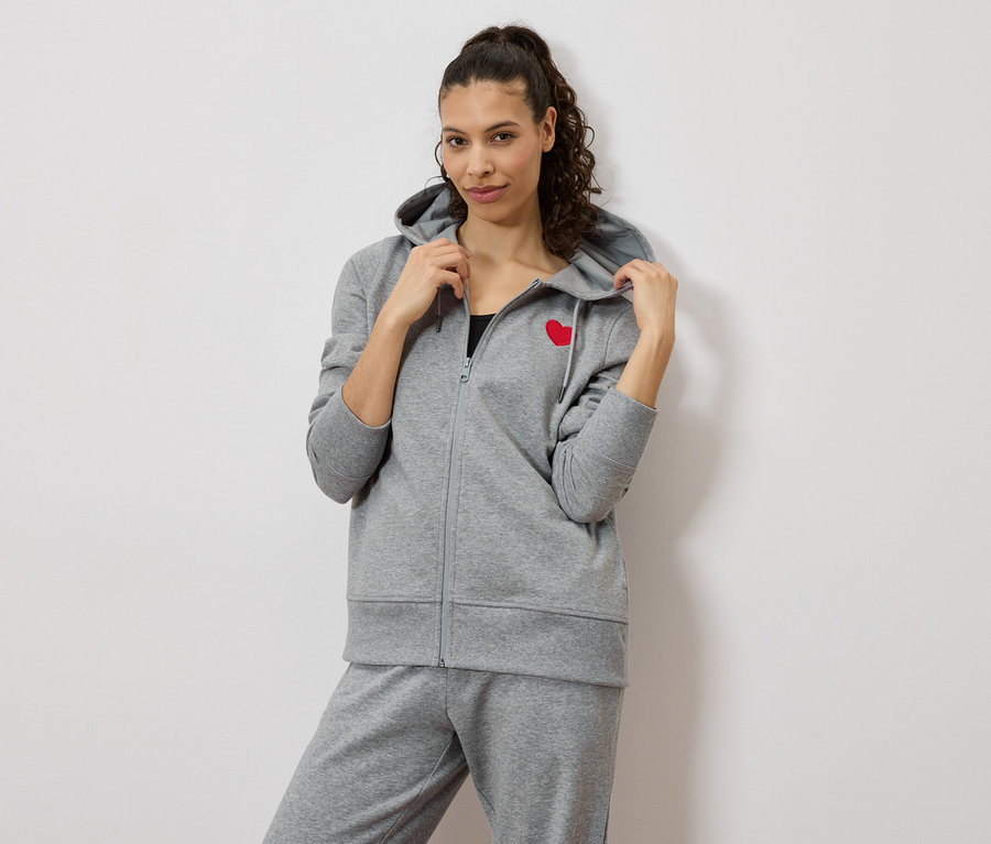 Femme portant un survêtement gris avec un cœur rouge sur la veste.