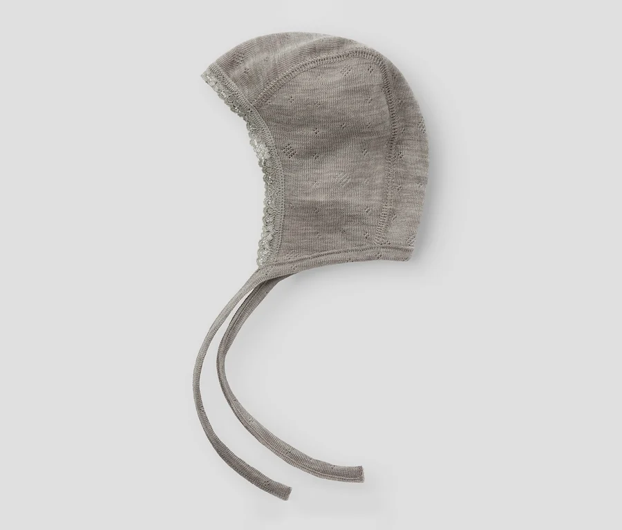 Bonnet de bébé tricoté gris avec bordure en dentelle et liens à nouer.