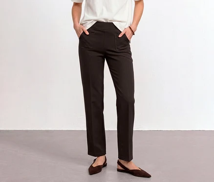 Une personne porte un pantalon en tissu Street One marron, les mains dans les poches, un t-shirt blanc et des chaussures plates marron.