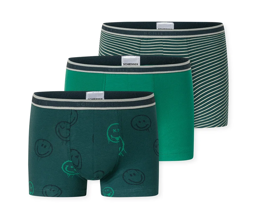 Trois shorts pour enfants SCHIESSER: un vert foncé à motifs de smileys, un vert moyen uni et un vert foncé à rayures blanches. Tous ont une ceinture SCHIESSER.