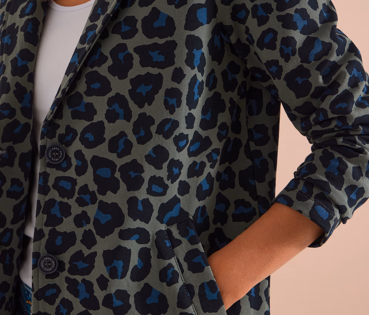 Personne portant un blazer en jersey à imprimé léopard vert, noir et bleu, la main dans la poche.