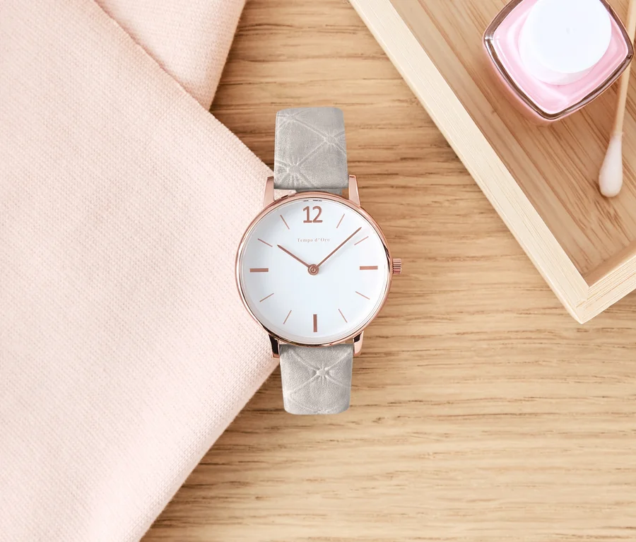 Une montre-bracelet avec bracelet en cuir est posée sur une table en bois à côté d'un tissu rose et de cosmétiques.