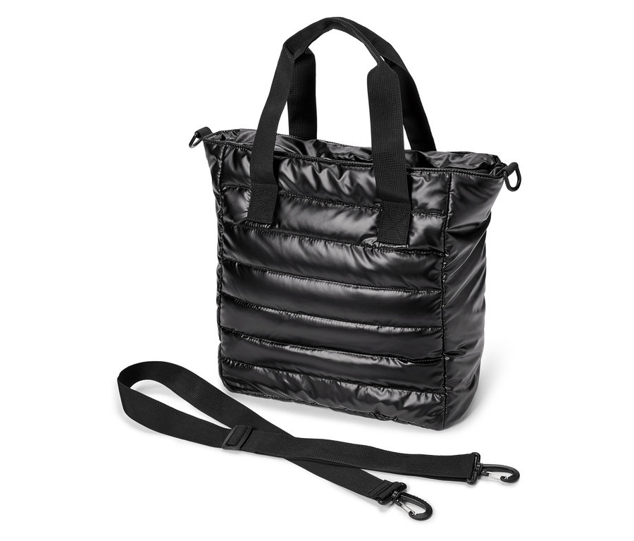 Un sac fourre-tout noir brillant matelassé avec des poignées noires et une bandoulière posé sur un fond blanc.