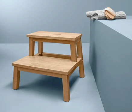 Un marchepied en hévéa est placé à côté d'une serviette grise et d'une brosse sur un fond bleu.