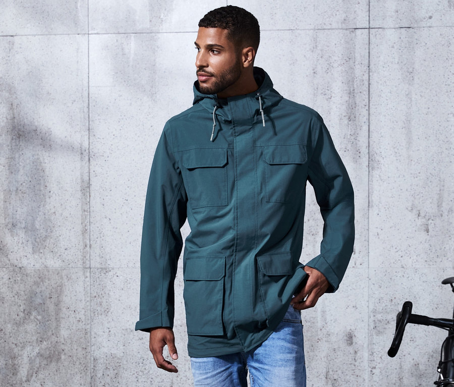 Un homme marche sur le trottoir et porte une parka fonctionnelle verte.